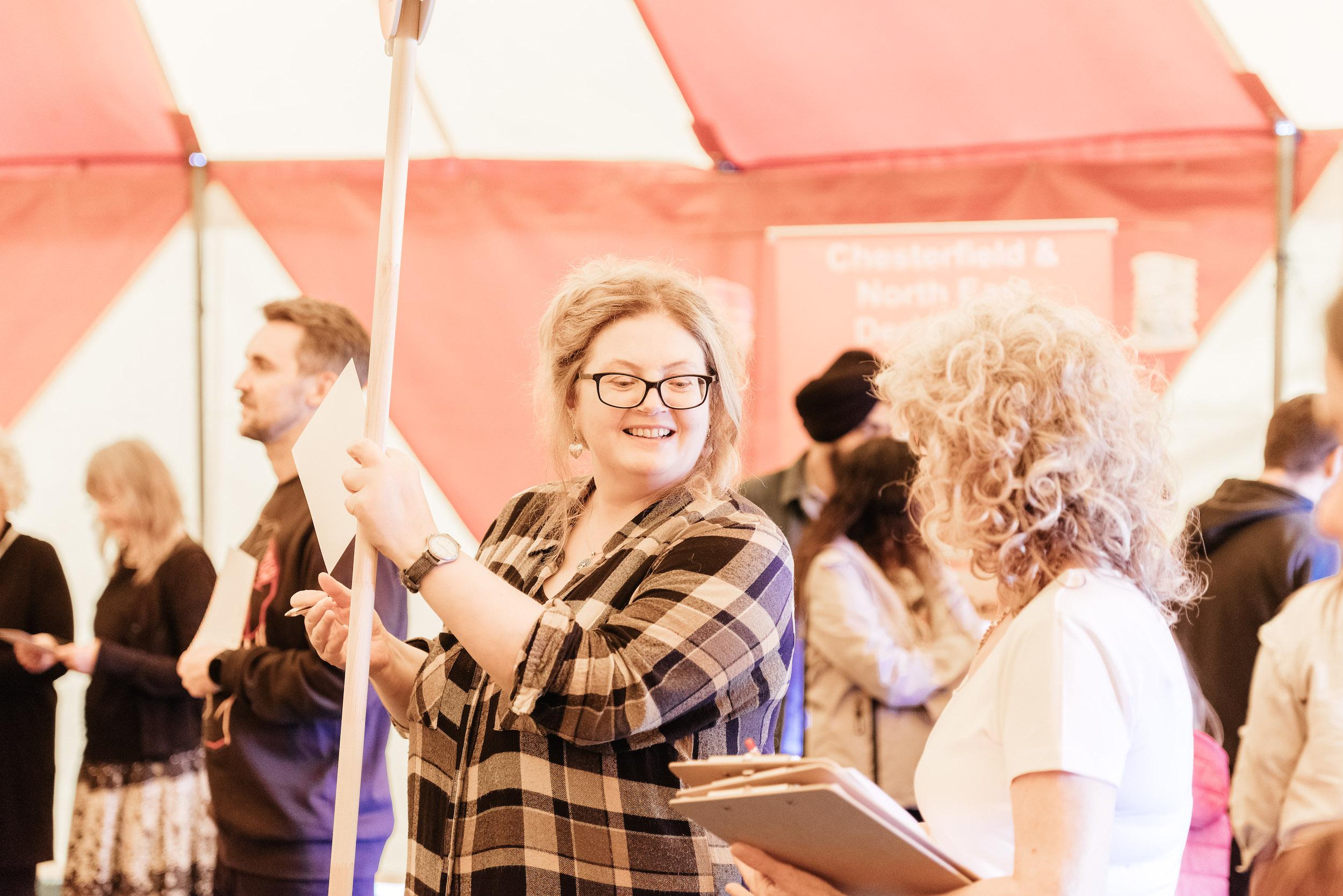 a woman wearing a checked shirt holding a lollipop sign inside a big top tent