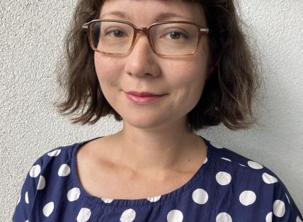 A woman with dark hair in a bob, wearing glasses and a blue and white spotty tshirt