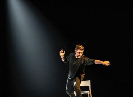 Lewis Doherty on stage with a chair and a beam of light