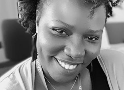 a black and white head and shoulders photo of Linda Ogallo a young black woman with mid length hair, wearing a dark top and lighter cardigan and an ICPAC lanyard