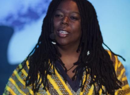 a black woman with long dark hair wearing a yellow and black dress