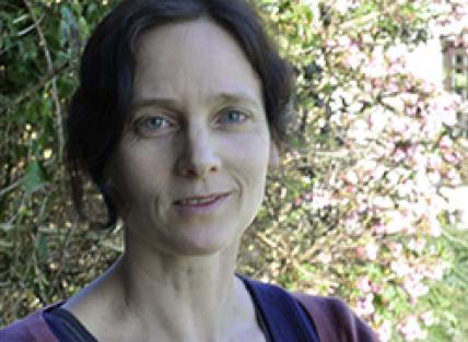  a white woman with dark hair tied back, wearing a purple jumper