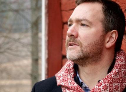 a white man with short brown hair and a beard, wearing a red and white scarf