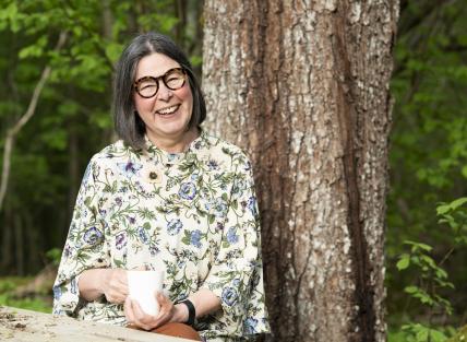 a white woman with shoulder length dark hair, wearing glasses and a floral shirt